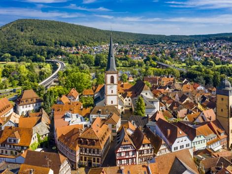 Luftaufnahme von Lohr am Main mit historischem Stadtkern, Kirchturm, roten Ziegeldächern, Fachwerkhäusern und bewaldeten Hügeln im Hintergrund.