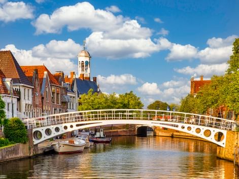 Weiße Fußgängerbrücke mit runden Öffnungen überspannt einen Kanal in Dokkum. Historische Gebäude mit orangefarbenen Ziegeldächern und Kirchturm säumen den Kanal.