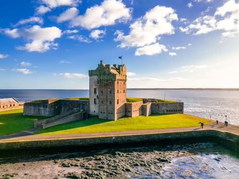 Broughty Castle in Dundee mit Steinturm und Befestigungen auf grüner Wiese neben Flussmündung unter blauem Himmel mit weißen Wolken.