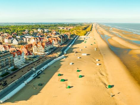 Luftaufnahme der Küstenstadt De Haan in Belgien mit traditioneller Architektur, breitem Sandstrand und Nordseeküste in der Ferne.