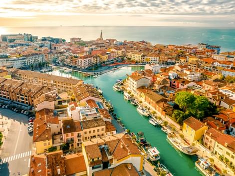 Luftaufnahme von Grado, Italien mit bunten Gebäuden und Terrakottadächern entlang eines Kanals zur Adria bei Sonnenuntergang.