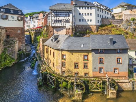Wasserfall, der durch historische Gebäude in Saarburg fließt. Traditionelle Fachwerkhäuser und Steinbauten umgeben den Wasserlauf.