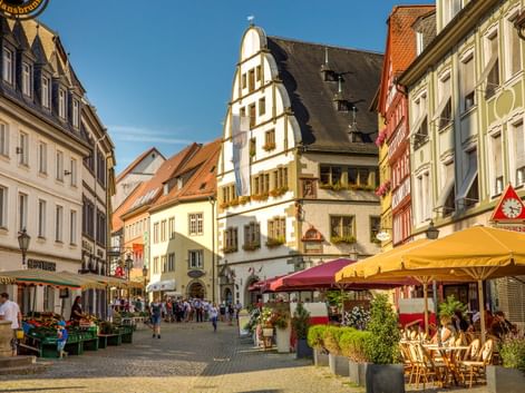 Fußgängerzone in Kitzingens Altstadt mit bunten Fachwerkhäusern, Straßencafés mit gelben Sonnenschirmen und Marktständen.