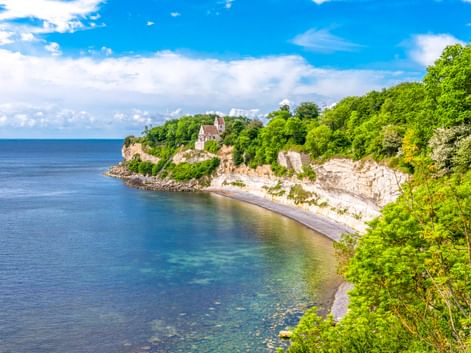 Weiße Kreidefelsen von Stevns Klint mit Højerup Kirche oben, umgeben von grünen Bäumen. Ein kleiner Strand verläuft entlang des blauen Meeres.