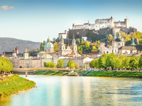 Salzburger Altstadt mit Festung Hohensalzburg auf dem Hügel, barocken Kirchenkuppeln und der Salzach mit grünen Ufern im Frühling.