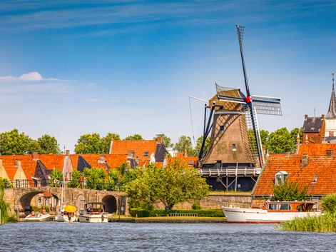 Traditionelle holländische Windmühle Molen De Kaai in Sloten mit orangefarbenen Ziegeldächern, Kanal mit Boot, Steinbrücke und Kirchturm.
