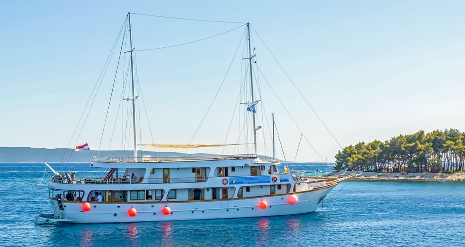 Weiße Motoryacht MS Amore mit zwei Masten und roten Fendern in ruhigen blauen kroatischen Gewässern, mit bewaldeter Küste im Hintergrund.