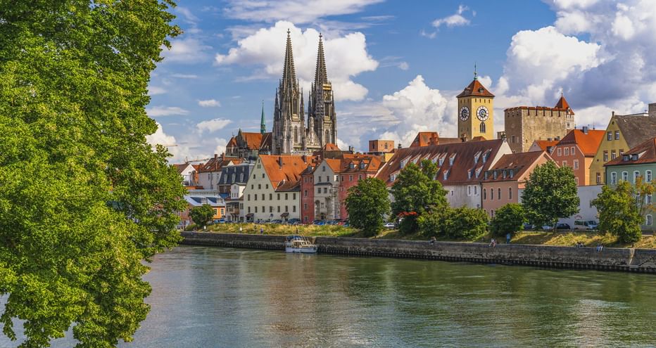 Regensburger Altstadt mit Domtürmen und mittelalterlichen Türmen an der Donau unter blauem Himmel mit weißen Wolken.