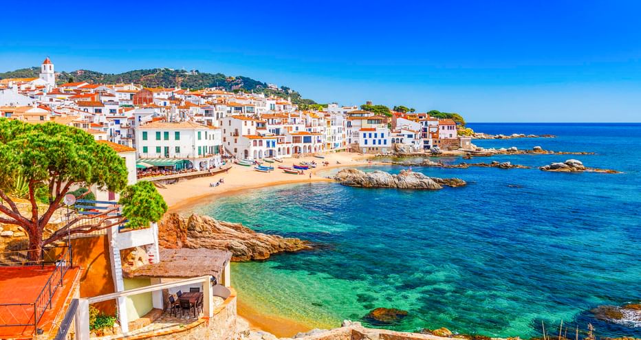 Calella de Palafrugell: weiße Häuser mit Terrakottadächern entlang Sandstränden und türkisfarbenem Mittelmeer mit Felsformationen.
