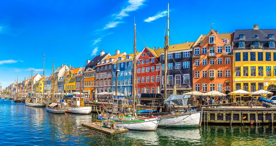 Historische Holzsegelboote am Nyhavn-Kanal in Kopenhagen mit bunten Stadthäusern aus dem 17. Jahrhundert unter blauem Himmel.