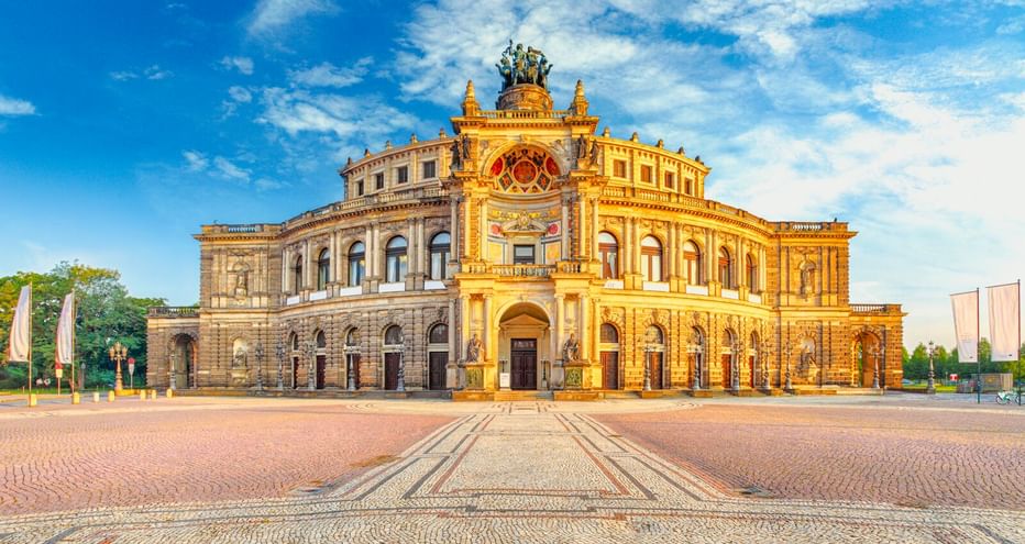 Die Semperoper in Dresden mit ihrer prächtigen Neorenaissance-Fassade im goldenen Sonnenlicht, mit Bogenfenstern und Skulpturen auf dem Dach.